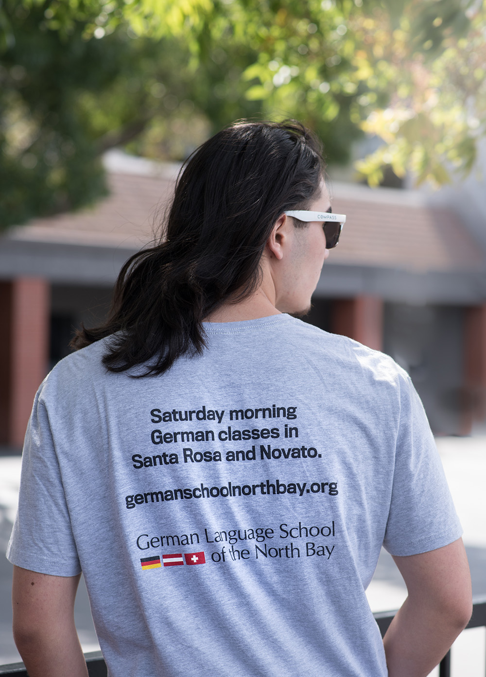 About_2026 High school student posing with the back of school shirt that says "Saturday morning German classes in Santa Rosa and Novato." as well as the website and school logo.